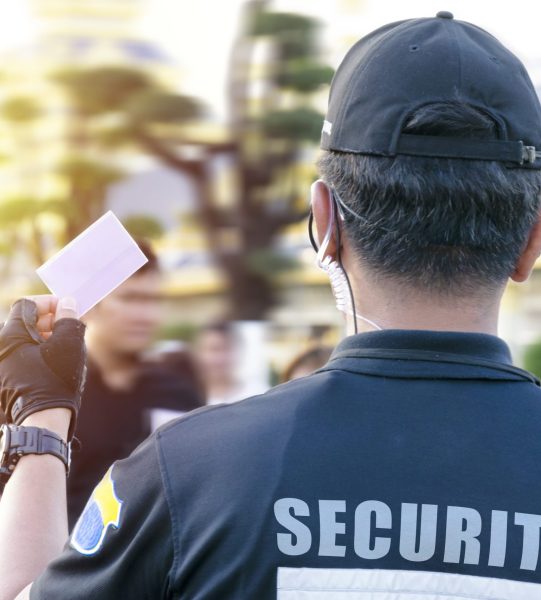 Male security guard using portable radio outdoors, label inscription on the uniform of the security guard.